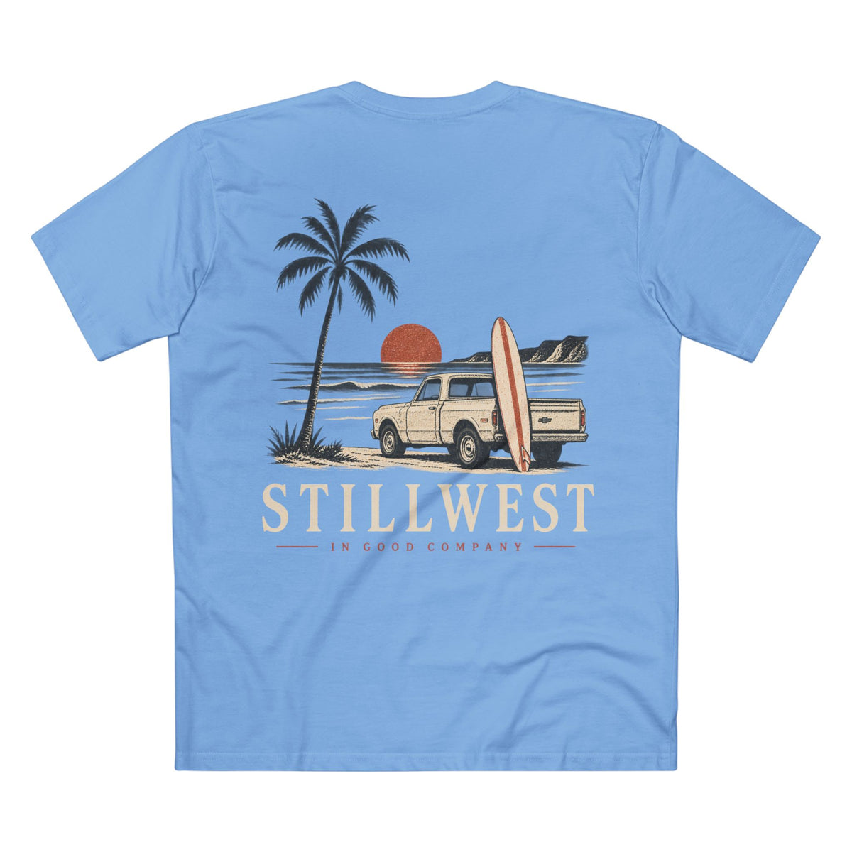 A light blue short-sleeve t-shirt shown from the back, featuring a retro-style graphic of a beach scene with a palm tree, a cream pickup truck carrying a surfboard, a red-orange sun, and the text 'STILLWEST IN GOOD COMPANY'.
