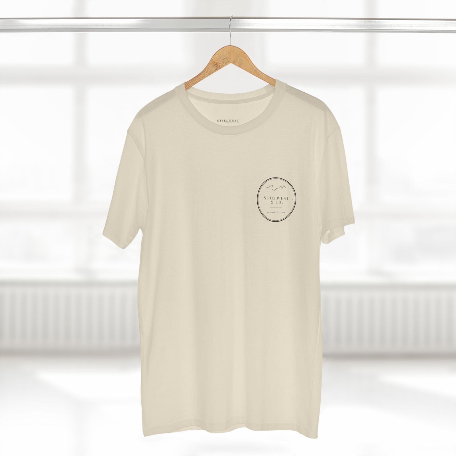 Beige t-shirt with a small black logo on a hanger against a white background
